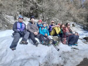 Na zdjęciu grupa osób siedzi na śniegu w lesie