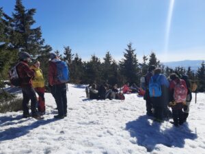 Na zdjęciu 3 grupy ludzi, stoją w śniegu lub siedzą i rozmawiają.