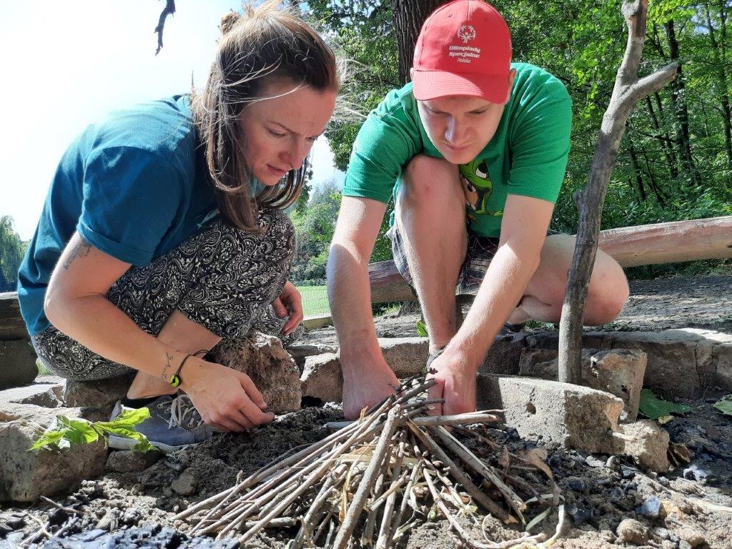 Dwie osoby rozpalają ognisko. Jedna z nich to Magda Kowalska z Fundacji Imago. Zdjęcie wykonane na zewnątrz, kiedy było ciepło.