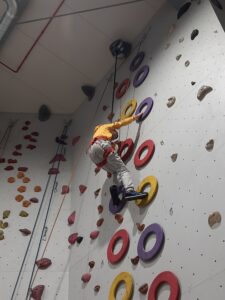 Na zdjęciu chłopiec, który wspina się na ściance wspinaczkowej po chwytach w kształcie kółek.