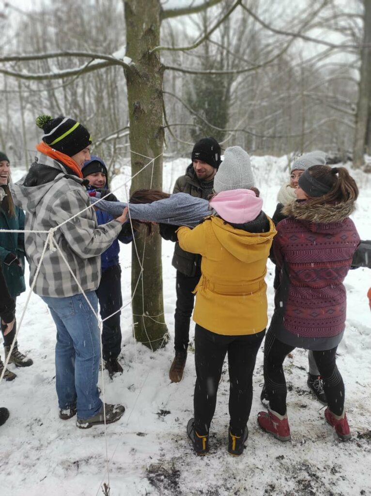 A group of people doing spider expercise between trees. Snowing around.