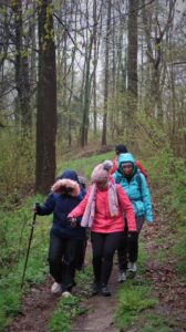 na zdjęciu 4 osoby ubrane w kurtki przeciwdeszczowe idące przez las ścieżką.