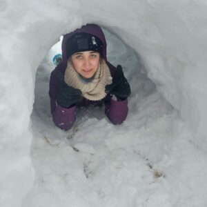 Na zdjęciu młoda dziewczyna leży w jamie śnieżnej.