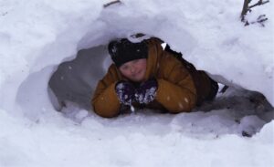 Na zdjęciu dziewczyna leży wewnątrz jamy śnieżnej.