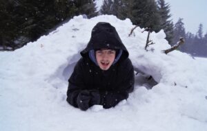 Na zdjęciu młody mężczyzna leży na śniegu. Jego górna część ciała wystaje z jamy śnieżnej.