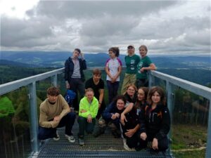 na zdjęciu grupa młodych ludzi z placakami stojących na platformie widokowej, za nimi panorama gór.