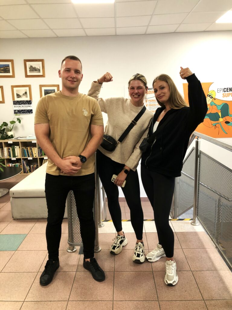 Troje przedstawicieli Stowarzyszenia Yava pozuje do zdjęcia w pomieszczeniu 3 sektora we Wrocławiu. Dwie kobiety podnoszą rękę pokazując „biceps” – symbol siły. Wszyscy uśmiechają się do zdjęcia.