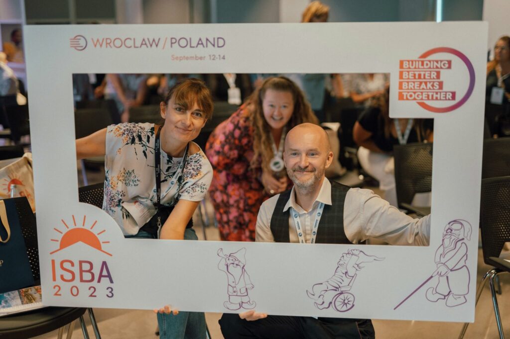 Specjalna ramka do zdjęć z napisem ISBA 2023. Wspólne zdjęcie robią sobie uśmiechnięci: Magda Stempska i Piotr Kuźniak z Fundacji Imago oraz przedstawicielka międzynarodowej organizacji zajmującej się opieką wytchnieniową.