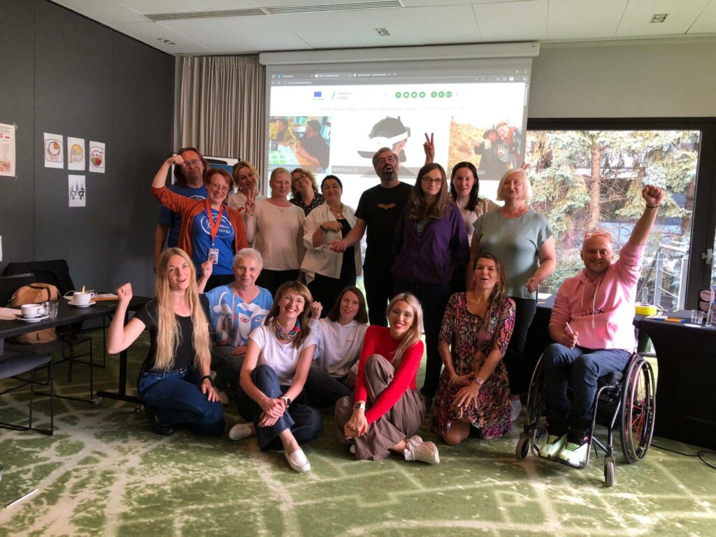 Zdjęcie w sali szkoleniowej projektu "Mam Tę Moc". Na zdjęciu jest 17 osób, uśmiechają się i unoszą ręce w górę, pozując do zdjęcia. Są to uczestnicy, prowadzący, eksperci biorący udział w projekcie "Mam Tę Moc".