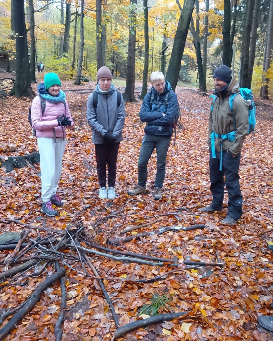 Cztery osoby stoją w półokręgu w lesie, zdjęcie wykonane jesienią.