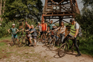 Na zdjęciu grupa młodych osób na rowerach pozująca przed wieżą widokową w lesie