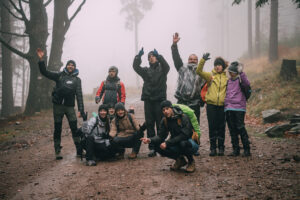 Na zdjęciu grupa szczęśliwych ludzi z rękami do góry w geście zwycięstwa. Osoby stoją na leśnej szerokiej drodze.