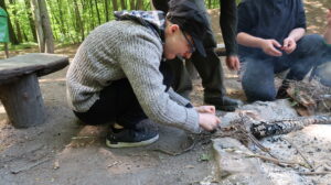 Na zdjęciu chłopak który próbuje rozpalic ogień krzesiwem w lesie.