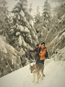 Dwie osoby i pies w zaśnieżonym lesie