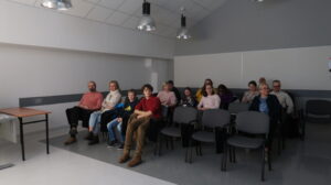 Na zdjęciu ludzie siedzący na krzesłach na sali wykładowej.