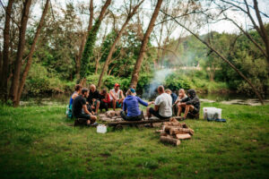 Na zdjęciu grupa młodych osób siedzi wokół ogniska w lesie