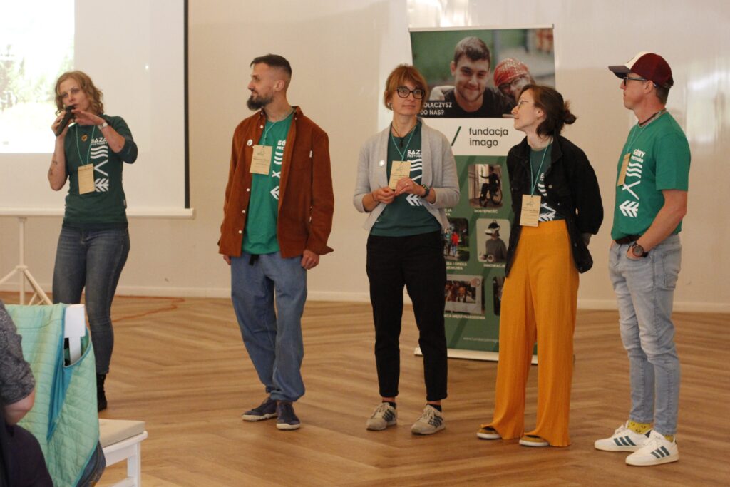 Organizatorzy konferencji "Natura bez Barier" stoją naprzeciwko uczestników, rozpoczynając konferencję. Na zdjęciu: Agata Włodarczyk - trzyma w ręku mikrofon, Wojciech Walkarz, Magda Stempska, Magda Kowalska, Michał Lemański. Wszyscy z Fundacji Imago.