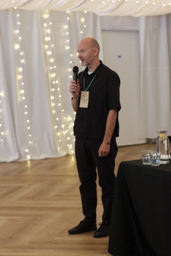 Sala konferencyjna, Piotr Kuźniak, prezes Fundacji Imago, przemawia, trzymając w ręku mikrofon. Rozpoczyna konferencję "Natura bez Barier".
