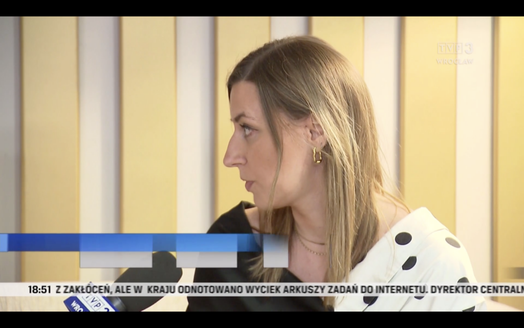 Skrin z ekranu komputera - kadr z programu "Fakty" TVP3 Wrocław. Na zdjęciu Martyna Rangno z Fundacji Imago odpowiada na pytanie, przed nią widoczyny mikrofon z kostką TVP3 Wrocław.