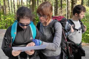 Na zdjęciu dwie kobiety w lesie patrzą wspólnie na mapę.