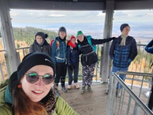 Zdjęcie selfie z wieży widokowej. Na zdjęciu grupa młodych osób w czapkach i z plecakami.