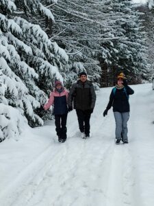 Na zdjęciu 3 osoby idące szlakiem górskim w zimie. Na ziemi i na drzewch leży dużo śniegu.