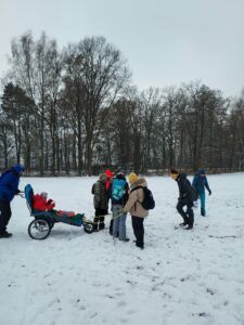 Na zdjęciu grupa osób szuka czegoś w śniegu ( tropów zwierząt)