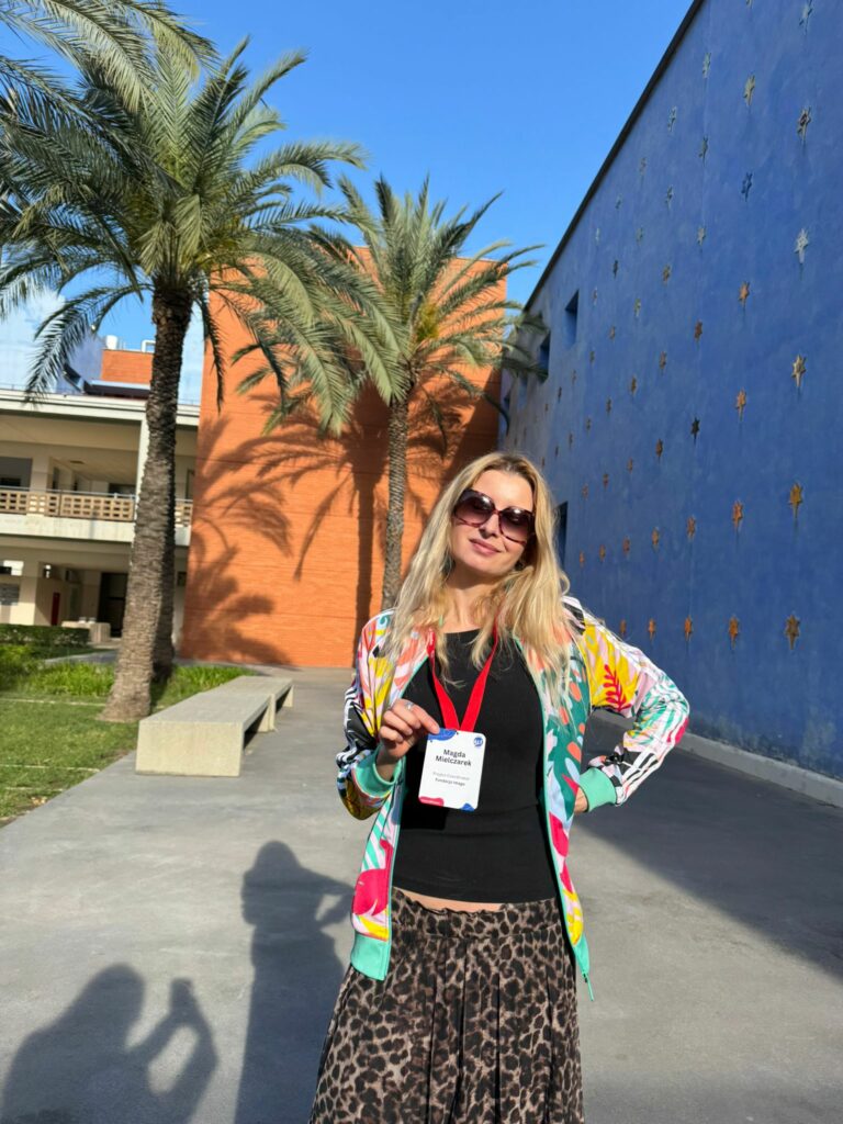 Magda Mielczarek z Fundacji Imago pozuje do zdjęcia przed budynkami, gdzie odbywa się konferencja.
