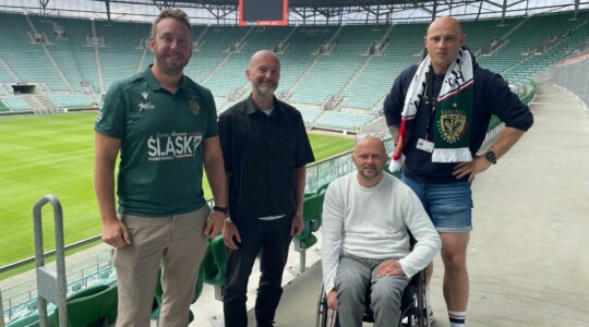 Zdjęcie wykonane na stadionie. Na zdjęciu są cztery osoby, które pozują do fotografii: Piotr Kuźniak i Łukasz Siemież z Fundacji Imago oraz Mateusz Jankowski i Marcin Ciarkowski z WKS Śląsk Wrocław.