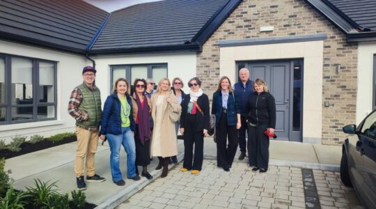 10-osobowa grupa pozuje do zdjęcia na świeżym powietrzu, w tle widać jednopiętrowy budynek. Wśród osób na zdjęciu są Martyna Rangno i Michał Lemański z Fundacji Imago.