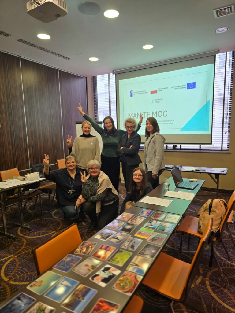 Uczestniczki i prowadzące szkolenie Mam tę moc w Opolu w sali szkoleniowej na tle ekranu z napisem "Mam tę moc" i logotypami szkoleniowymi. Podnoszą ręce w geście zwycięstwa.