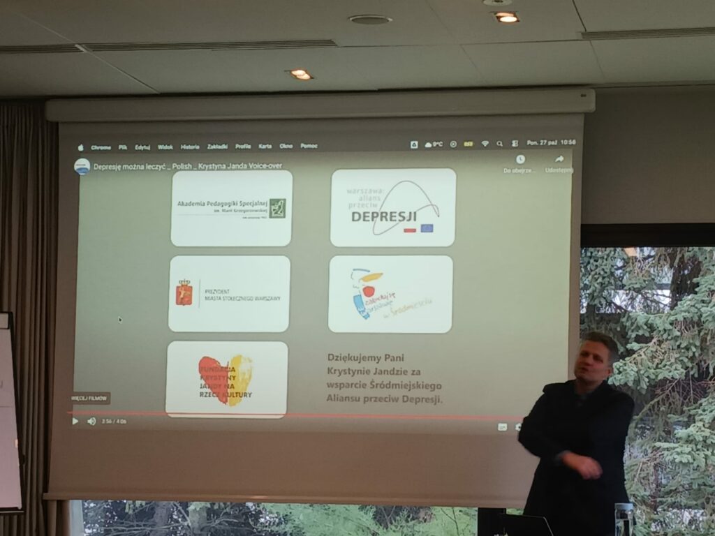 Spotkanie grupy roboczej projektu MOC w sali szkoleniowej. Na zdjęciu jest dr Piotr Toczycki stojący przy dużym ekranie, na ekranie w oczy rzuca się napis "depresja".