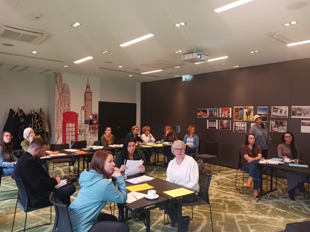 Spotkanie grupy roboczej projektu MOC w sali szkoleniowej. Kilkunastu uczestników i uczestniczek szkolenia siedzi przy stolikach.