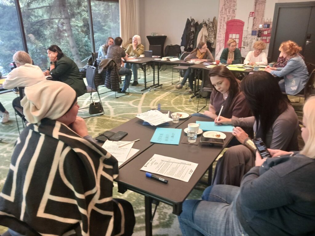 Spotkanie grupy roboczej projektu MOC w sali szkoleniowej. Kilkunastu uczestników i uczestniczek szkolenia siedzi przy stolikach.