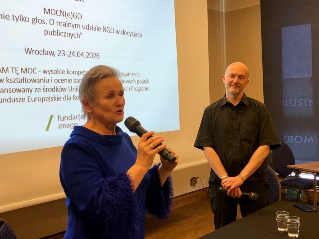 Sala konferencyjna. Przed ekranem z prezentacją stoi Alicja Szatkowska z mikrofonem, obok Piotr Kuźniak. Alicja Szatkowska wygłasza wykład.