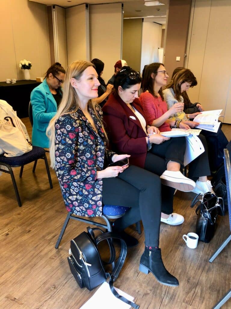 Sala konferencyjna. Uczestnicy konferencji słuchają prezentacji i notują.