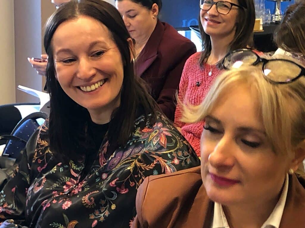 Sala konferencyjna. Uczestniczki konferencji, wśród nich jest uśmiechnięta Basia Górka z Fundacji Imago. 