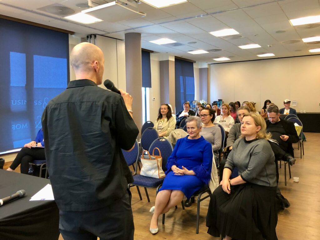 Sala konferencyjna. Uczestnicy konferencji słuchają Piotra Kuźniaka z Fundacji Imago, który podsumowuje projekt “Mam Tę Moc”.