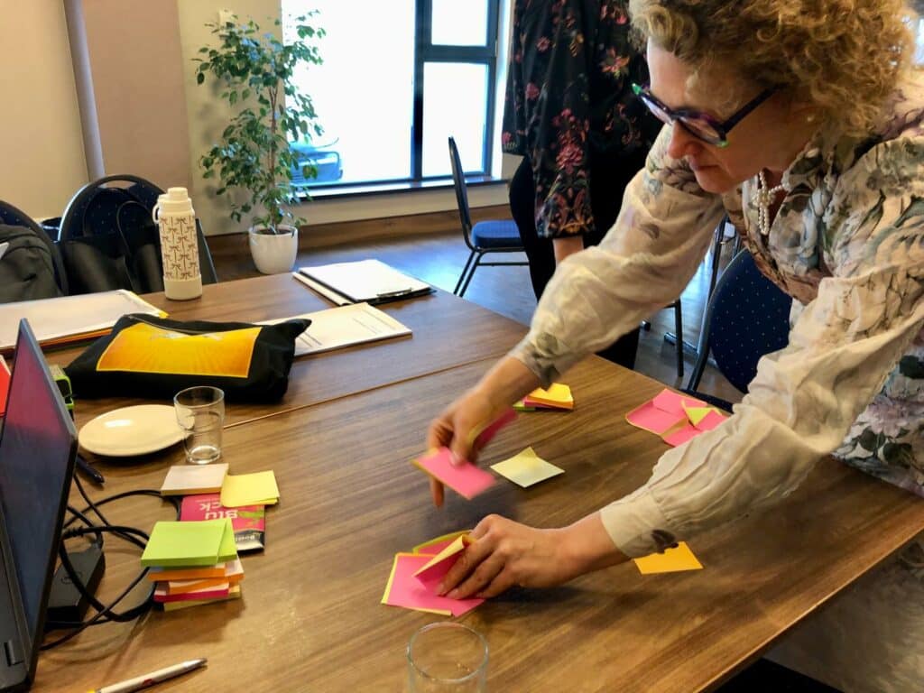Zdjęcie z sali konferencyjnej. Stolik, na nim rozłożone kolorowe karteczki. Anna Janus z Fundacji Imago bierze karteczki do ręki. 