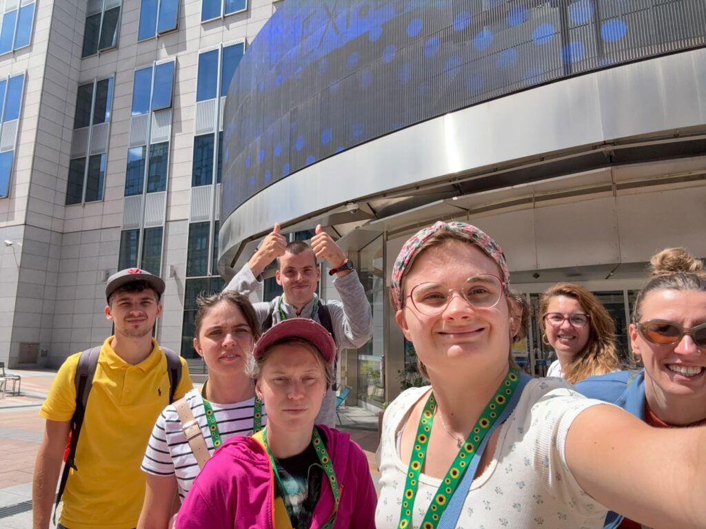 7-osobowa grupa pozuje do zdjęcia na tle budynków w Brukseli. To uczestnicy, wolontariusze i koordynatorzy projektu "Points of konekszyn".