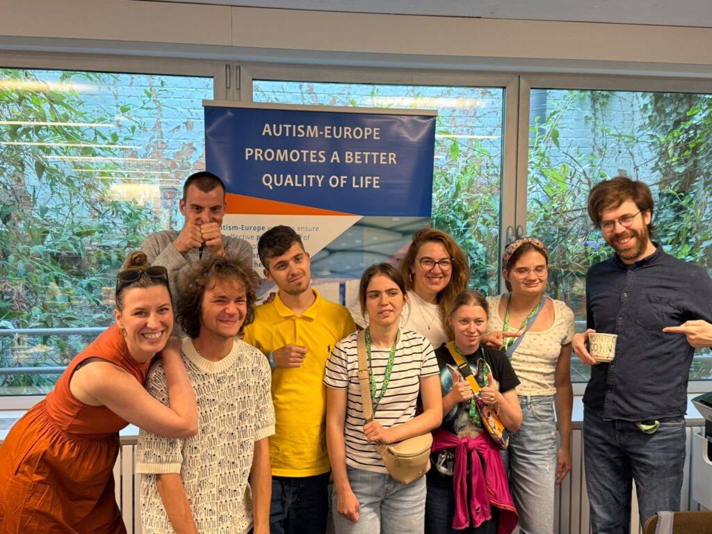 9-osobowa pozuje do zdjęcia. To uczestnicy, wolontariusze i koordynatorzy projektu "Points of konekszyn". Za nimi duży napis: "Autism Jurop promouts a better kłolity of lajf".