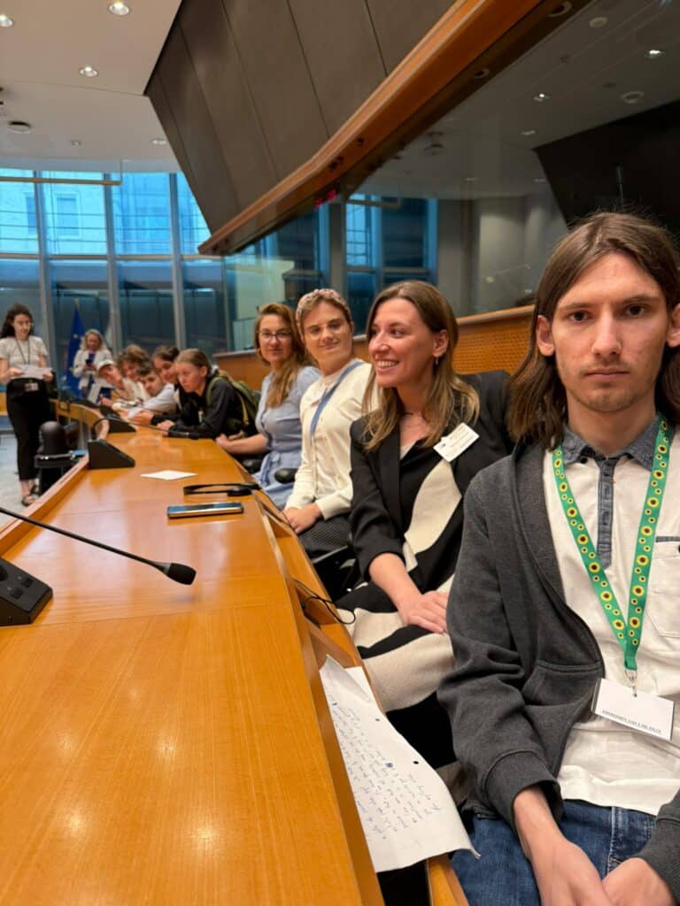 Zdjęcie zrobione we wnętrzu Parlamentu Europejskiego w Brukseli. Na zdjęciu, przy charakterystycznym dla parlamentu półokrągłym stole, siedzi grupa osób, wśród nich Martyna Rangno z Fundacji Imago oraz grupa młodych osób ze spektrum autyzmu, która wzięła bierze udział w projekcie Points of konekszyn.