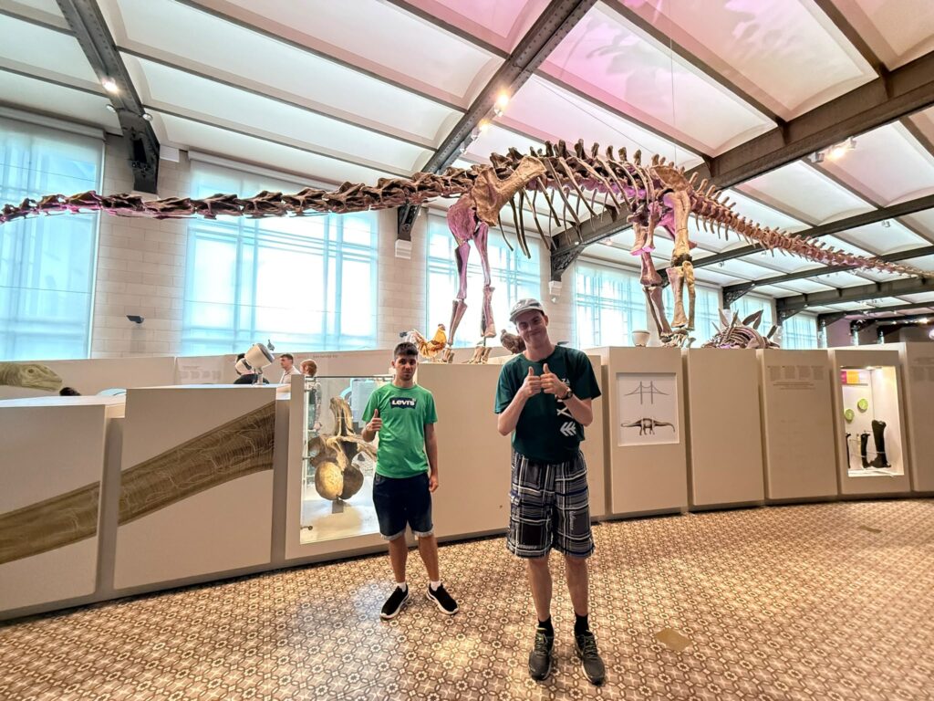 Dwaj uczestnicy polskiej grupy projektu Points of konekszyn pozują do zdjęcia w Muzeum Historii Naturalnej w Brukseli przy szkielecie dinozaura.