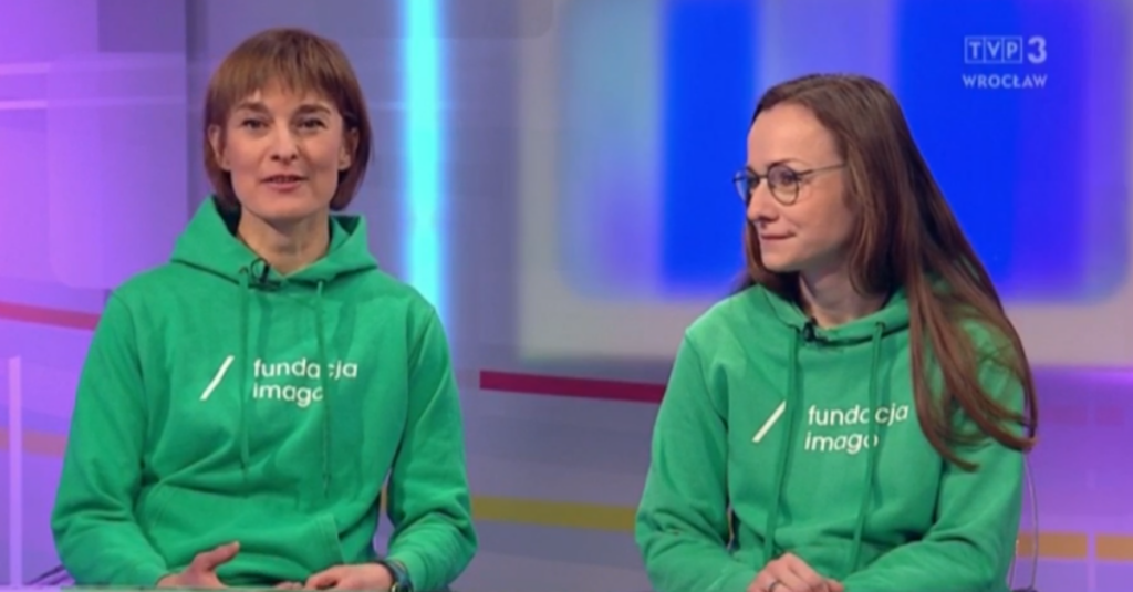 Zdjęcie wykonane w studiu Faktów o poranku TVP3 Wrocław. Magdalena Stempska i Magdalena Kowalska w czasie rozmowy. Mają na sobie zielone bluzy z białym logotypem Fundacji Imago.