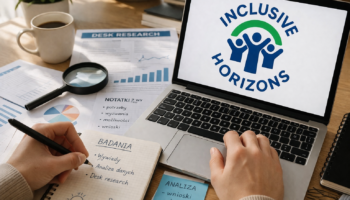 Biurko, na biurku notatki i ekran komputera z wyświetlonym logotypem projektu Inklusif Horizons. Na zdjęciu widać też ręce osoby siedzącej przy komputerze.