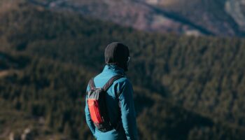Mężczyzna w ubraniach trekkingowych na tle gór. Jest odwrócony plecami do zdjęcia.